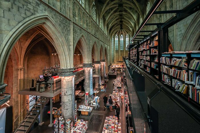 Grandiose library interior with vaulted ceilings, stone arches, and rows of bookshelves filled with books and visitors browsing.