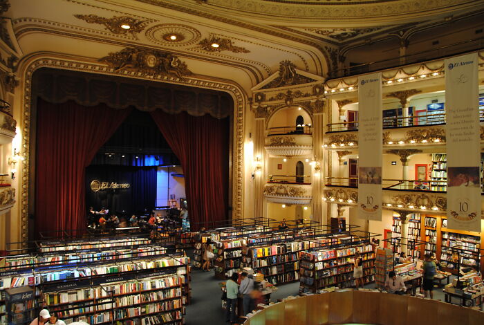 Grandiose library interior with ornate balconies and bookshelves filled with numerous books and visitors browsing.