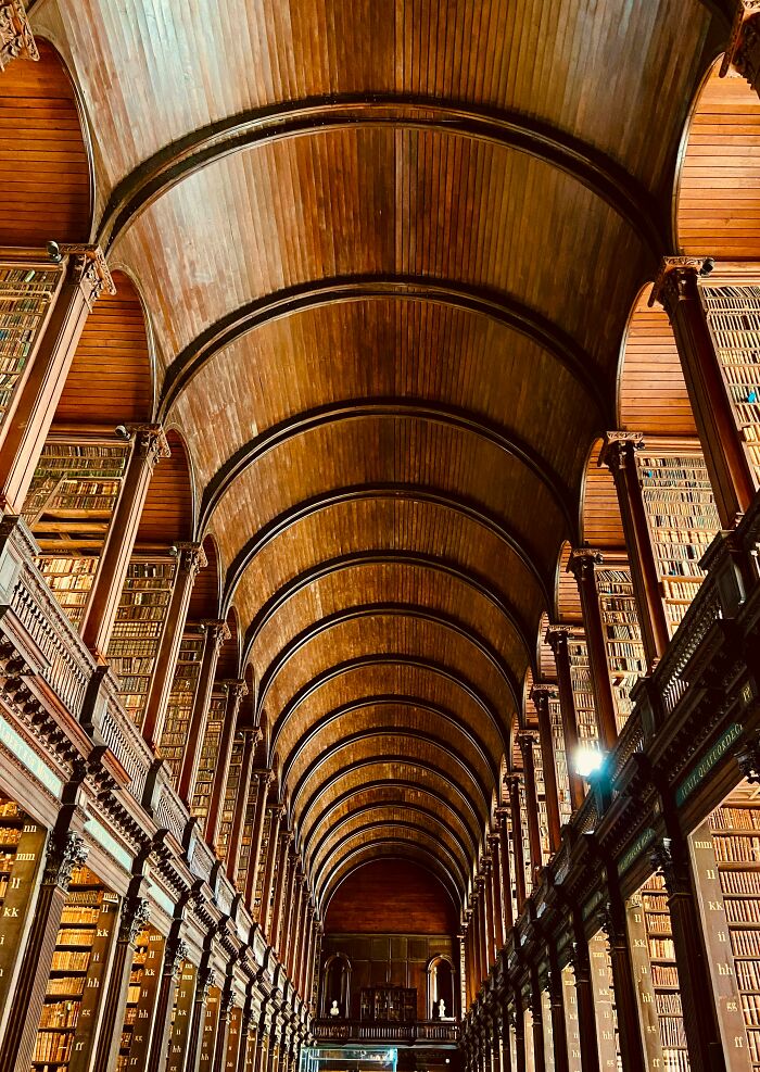 Grandiose library interior with high wooden vaulted ceiling and tall bookshelves filled with books from floor to ceiling.